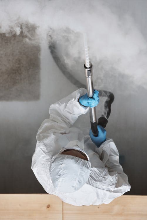 Pest control technician in protective gear spraying treatment inside a home